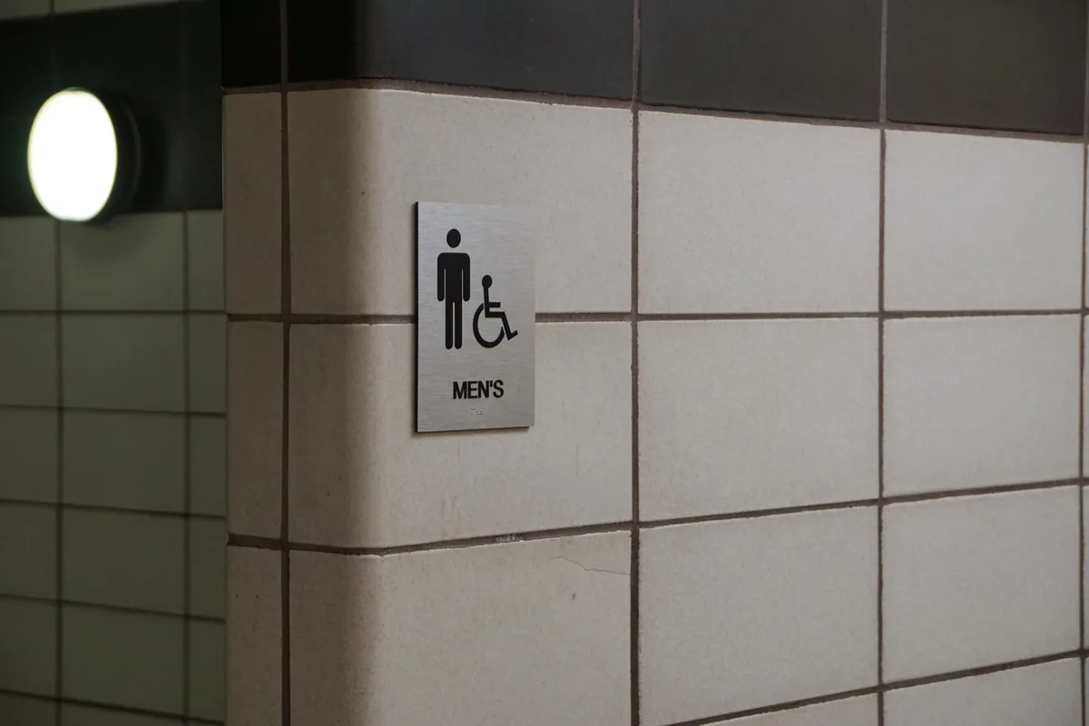 ADA-compliant restroom sign with tactile lettering and Braille, an example of office signage Austin building owners must meet under ADA room-ID rules